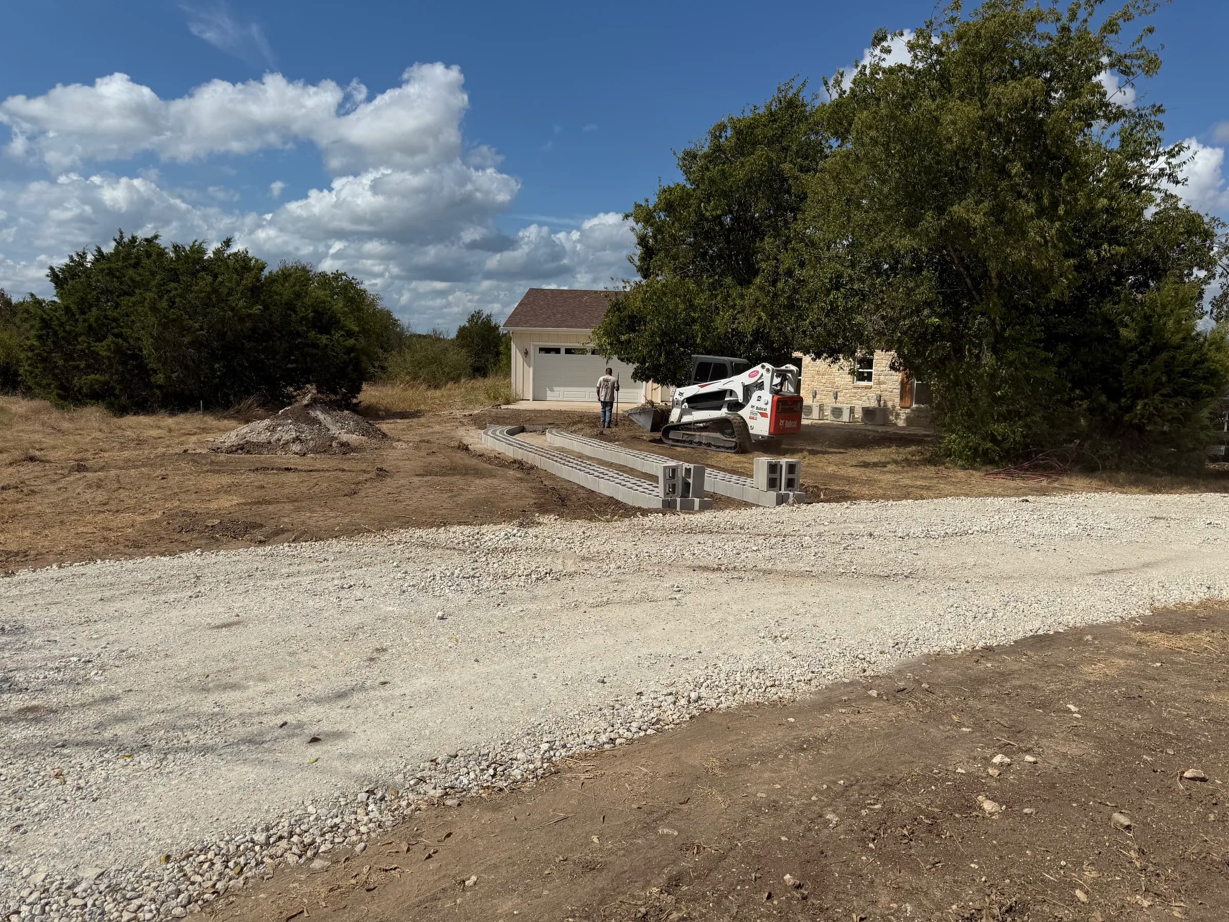 White Hall driveway installation with curved concrete blocks and a skid steer beside the gravel access road