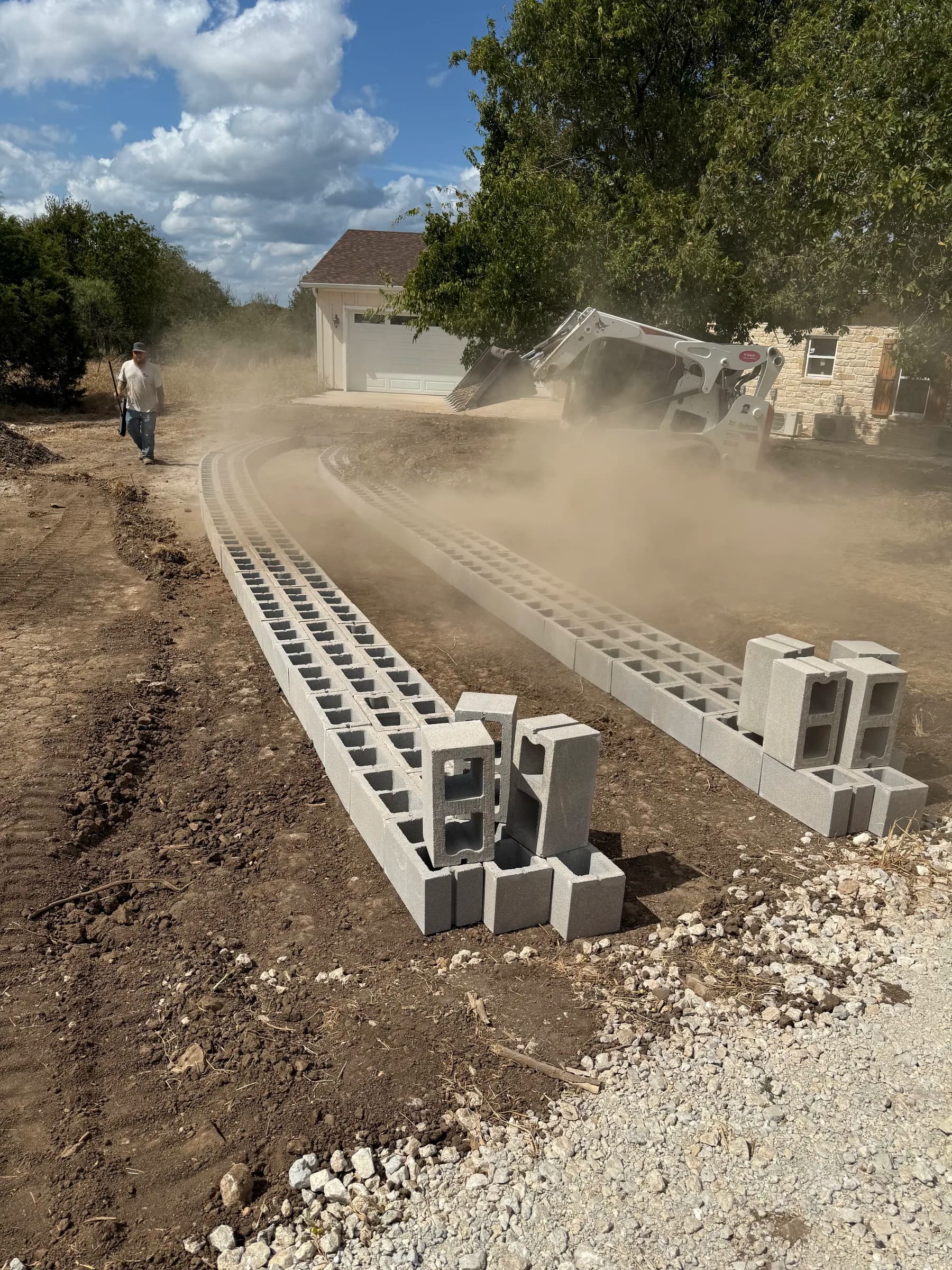 Driveway work in progress at White Hall, with curved concrete blocks, a crew member, and a skid steer