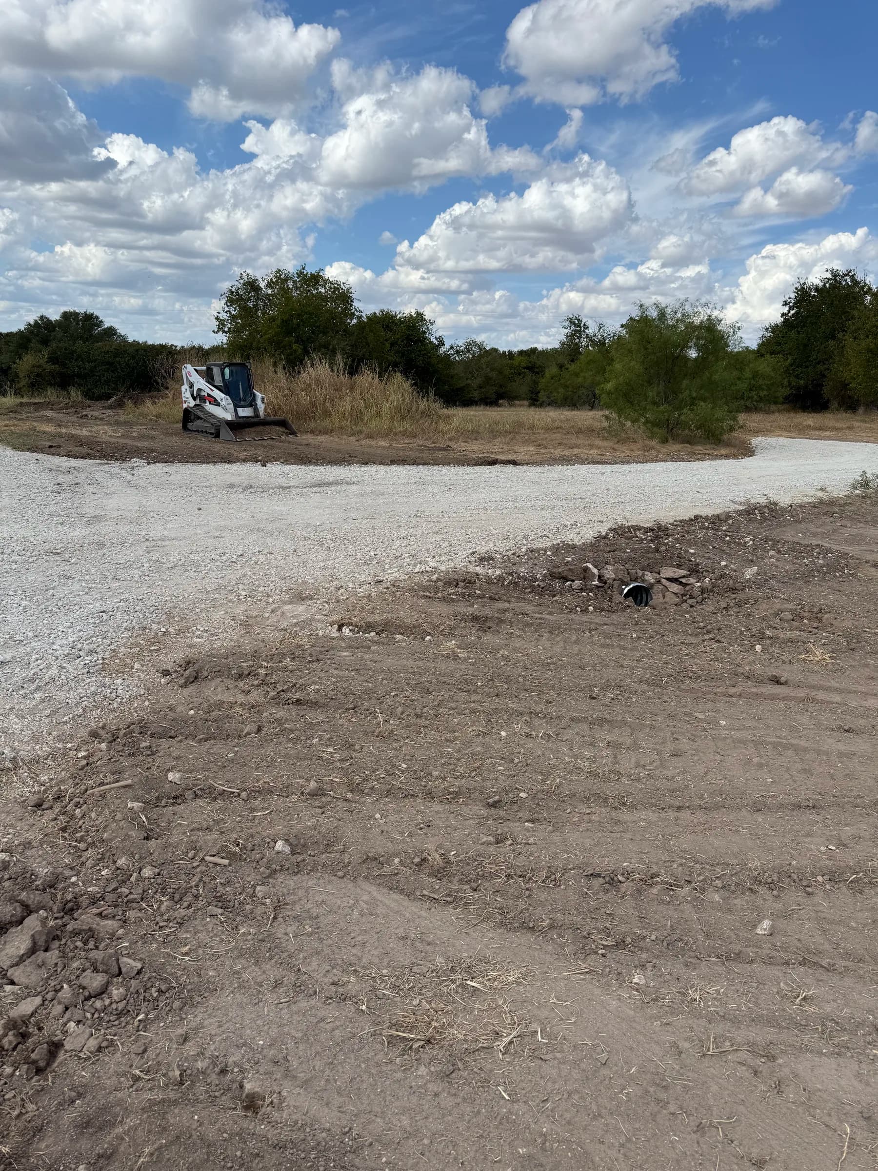 Gravel access crossing at White Hall with a visible culvert outlet and surrounding graded ground