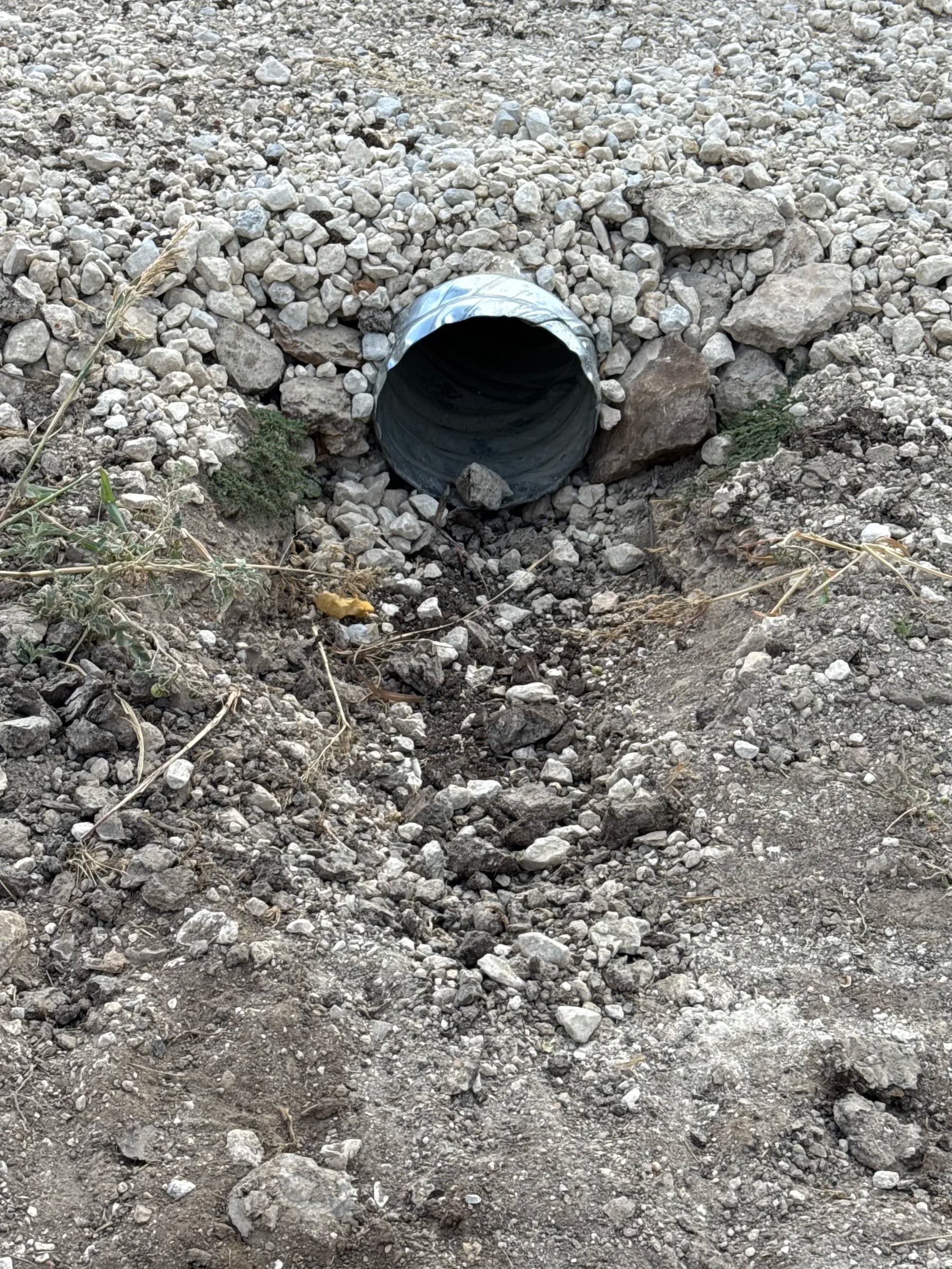 Close view of a corrugated culvert outlet surrounded by rock beneath the gravel crossing
