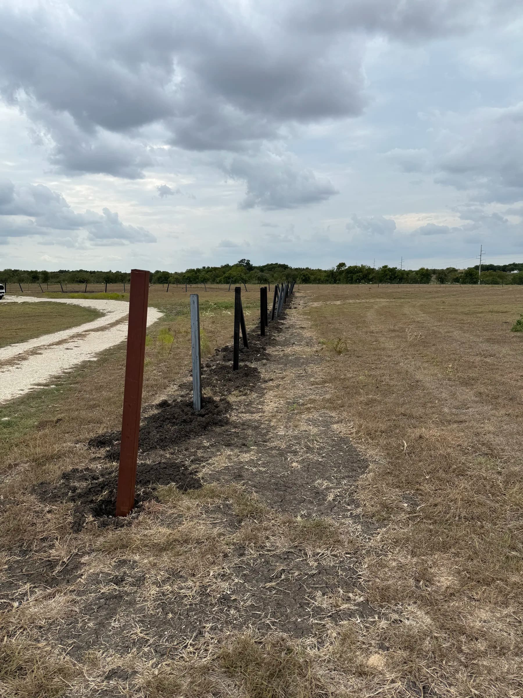 Steel fence posts set in a line beside the gravel drive during installation in Holland