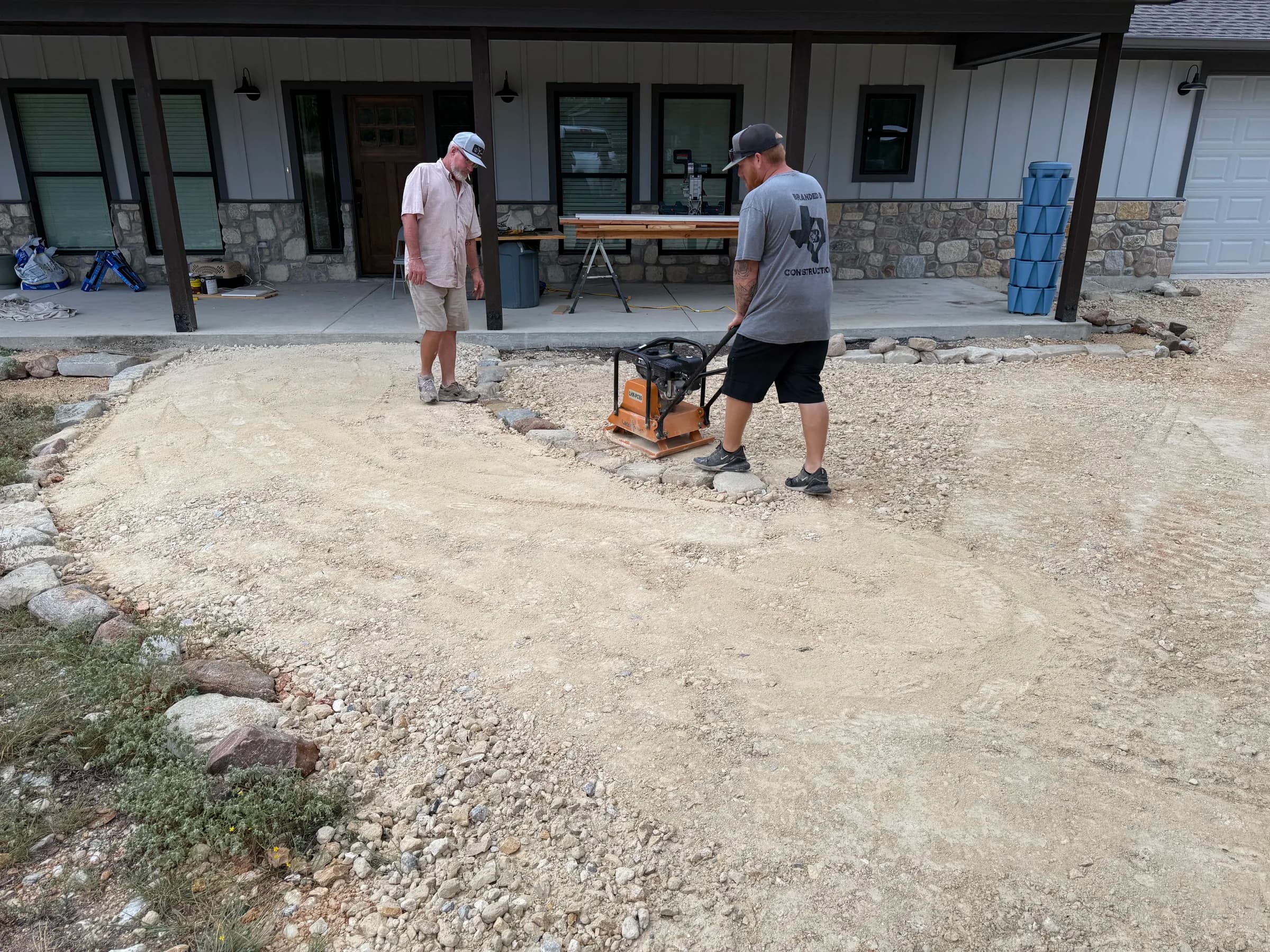 Branded B crew preparing and compacting a gravel area beside a home
